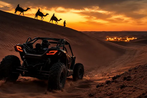 CAMEL + DUNE BUGGY Dune buggy below a camel trek silhouette on Lahbab red dunes at sunset