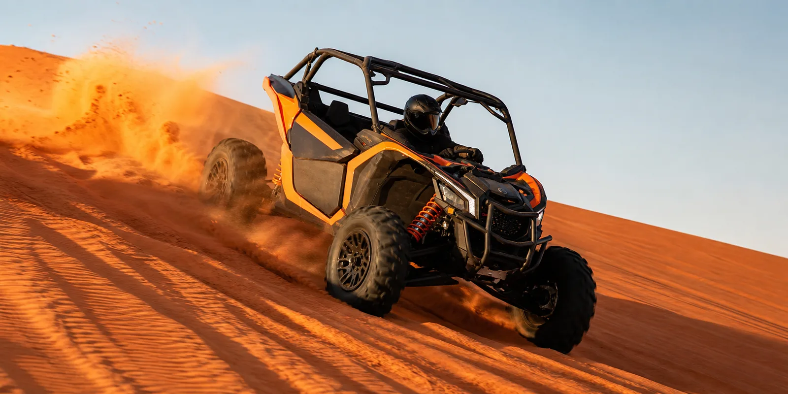 Dune buggy carving down a steep red Lahbab dune in a spray of sand at golden hour