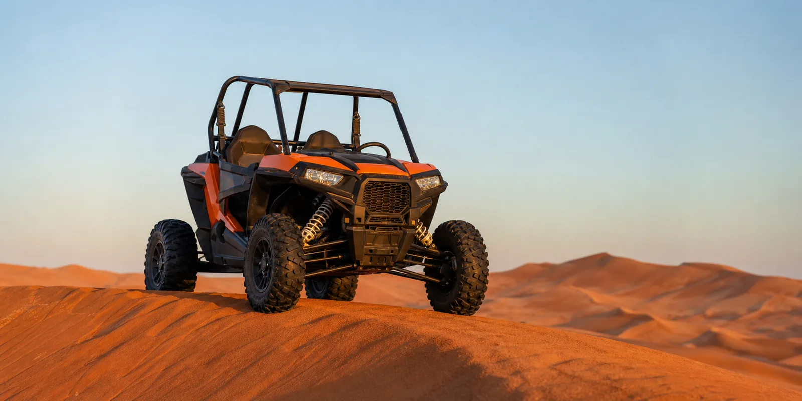 Orange Polaris RZR dune buggy parked on a red Lahbab dune crest at golden hour in Dubai