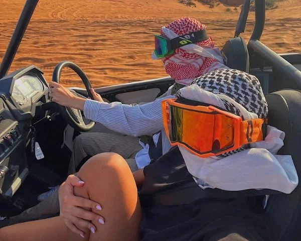 Silhouette of three dune buggies lined up on a desert dune crest against a vivid Dubai sunset sky