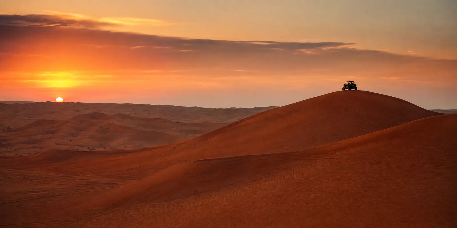 Lahbab red dunes at sunset with a lone dune buggy cresting a distant ridge